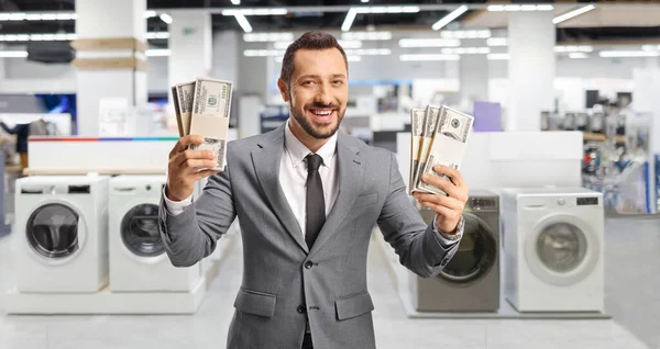 電気器具店の中でお金と笑顔を持っている若いビジネスマン — ストック写真