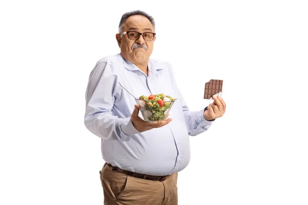 有疑问的成熟男人 手里拿着沙拉和巧克力棒 背景是白色的 — 图库照片