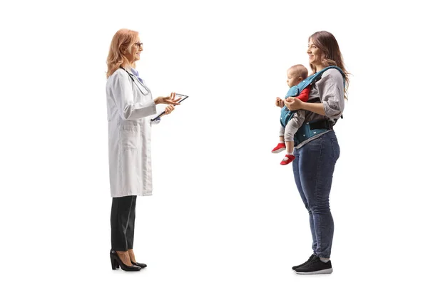 白い背景に隔離された赤ん坊を持つ母親と話している女性医師の完全な長さのプロフィールショット — ストック写真