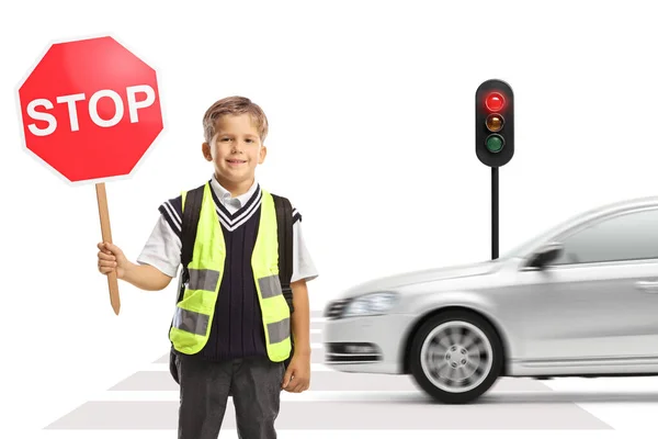 後ろに車を運転して横断歩道に立つ安全ベストと停止交通標識を持つ学校の少年 — ストック写真