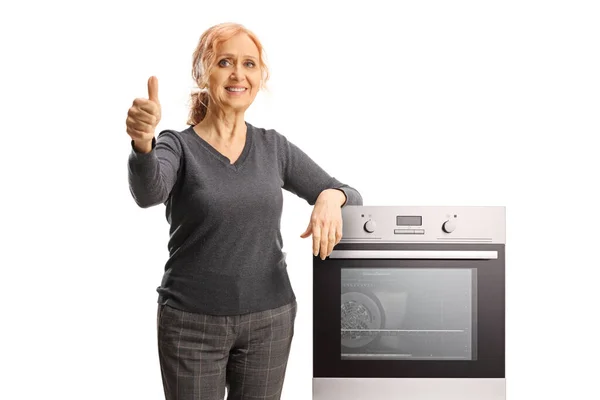 正在微笑的成熟女人靠在烤箱上 把大拇指伸出来 与白色背景隔离 — 图库照片