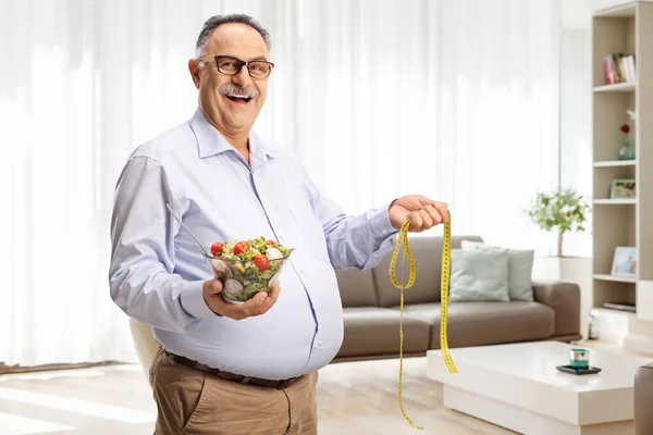 Volwassen Man Met Een Salade Een Meetlint Een Woonkamer — Stockfoto