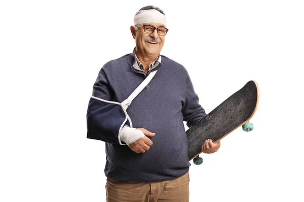 Зрелый Мужчина Сломанной Рукой Повязкой Голове Держащий Скейтборд Улыбающийся Изолированный — стоковое фото