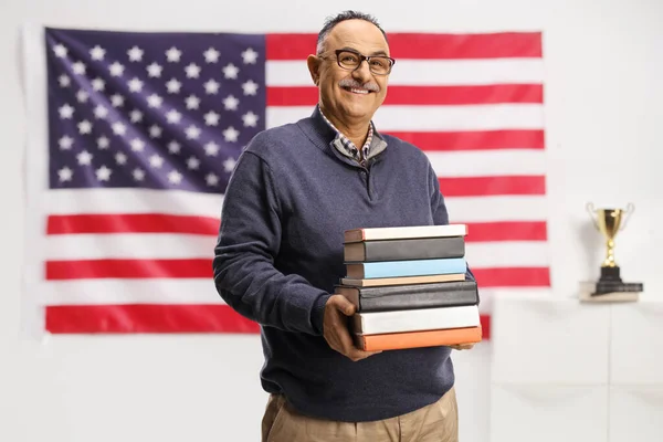 Uśmiechnięty Dojrzały Mężczyzna Trzymający Stertę Książek Pozujący Przed Flagą Usa — Zdjęcie stockowe