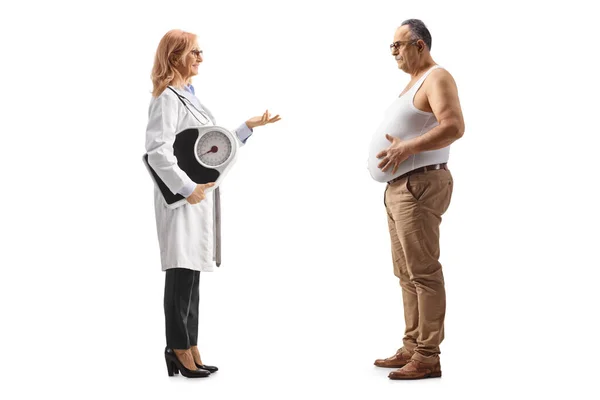 体重計を持っている女性医師の完全な長さプロファイルショットと話をします太りすぎ成熟した男に隔離された白い背景 — ストック写真