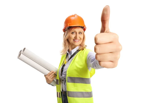 安全ベストとハードハットを持つ笑顔の女性エンジニア設計図を保持し 親指をジェスチャーアップ白の背景に隔離 — ストック写真