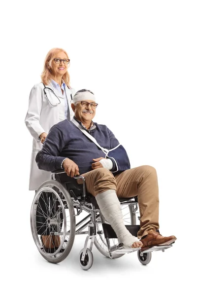 白い背景に隔離された後ろに立っている車椅子と女性医師に座って頭の上に壊れた腕と包帯を持つ熟女 — ストック写真