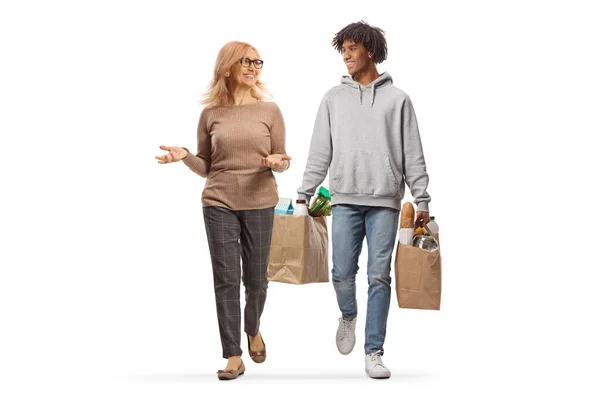 白人の背景に隔離された食料品袋を持つアフリカ系アメリカ人の若い男と歩くと話している白人女性の完全な長さの肖像画 — ストック写真