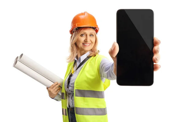 安全ベストとハードハットの設計図を保持し 白い背景に隔離されたスマートフォンを示す女性エンジニア — ストック写真