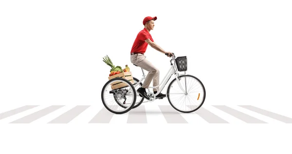 在一个白色背景隔离的人行横道上 送货员骑着一辆装有一箱水果和蔬菜的三轮车 — 图库照片