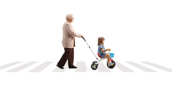 一个祖母用三轮车把小孩推倒在被白色背景隔离的人行横道上的全景照片 — 图库照片