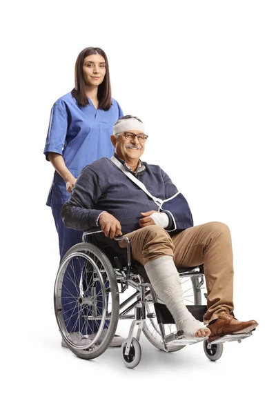 白い背景に隔離された車いすの上で腕と包帯を骨折した成熟した男と一緒に立っている看護師 — ストック写真