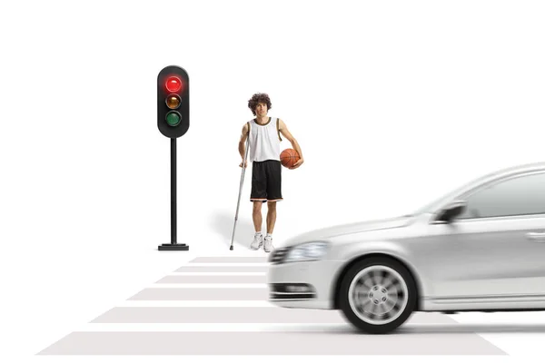 白地に隔離された道路を横断する信号待ちの松葉杖を持つバスケットボール選手 — ストック写真