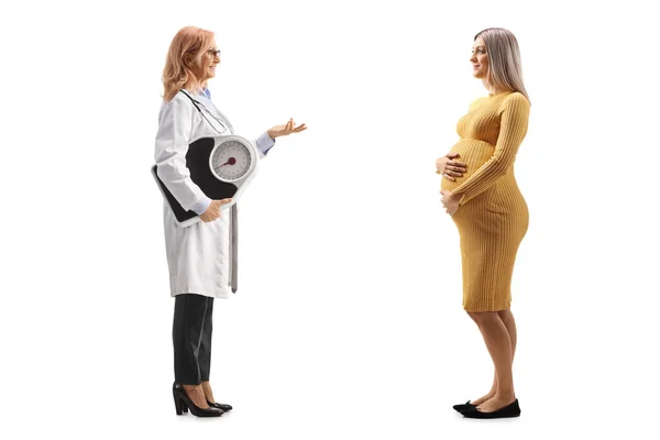 一名女医生举着举重刻度 与一位因白人背景而与之隔离的孕妇交谈时拍摄的全景照片 — 图库照片