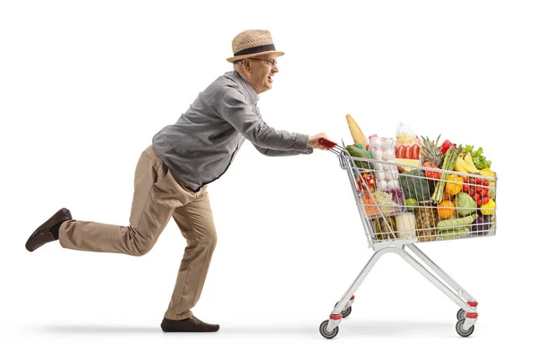 白い背景に孤立したショッピングカートで走っている高齢者の完全な長さのショット — ストック写真