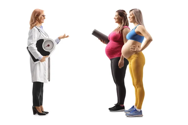 体重計を持っている女性医師の完全な長さのプロフィールショットと白の背景に隔離された2人の妊婦と話す — ストック写真
