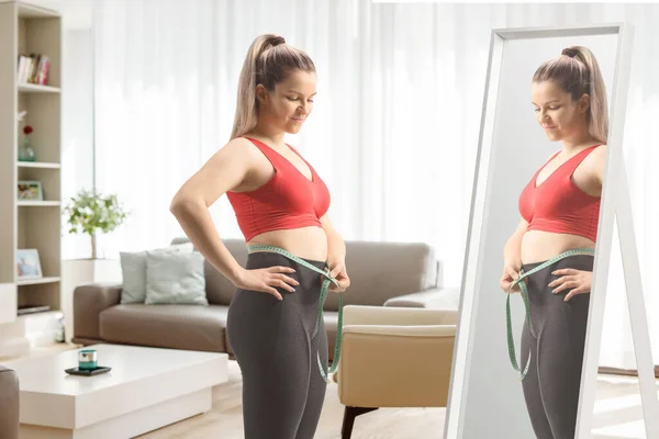 鏡の前に立つスポーツウェア姿の若い女性と 自宅のリビングルームで腰を測定 — ストック写真