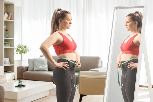 鏡の前に立つスポーツウェア姿の若い女性と 自宅のリビングルームで腰を測定 — ストック写真
