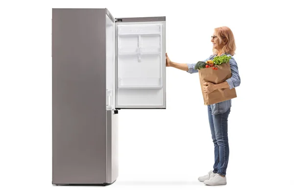Frau Mit Einkaufstasche Blickt Auf Leeren Kühlschrank Auf Weißem Hintergrund — Stockfoto