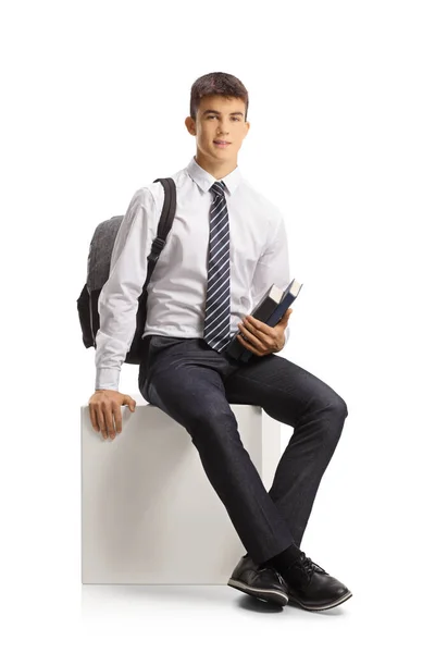 男子学生で学校制服保持本と座っている上に白の背景に隔離された白いキューブ — ストック写真