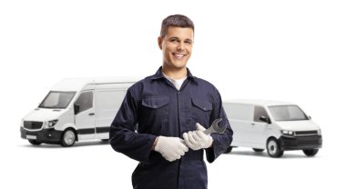 Gülümseyen tamirci İngiliz anahtarı tutuyor ve beyaz arka planda izole edilmiş iki beyaz minibüsün önünde duruyor.