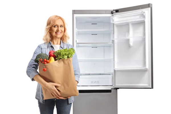 白い背景に隔離されたオープン空の冷蔵庫の前でポーズをとる食料品袋を持つ女性 — ストック写真