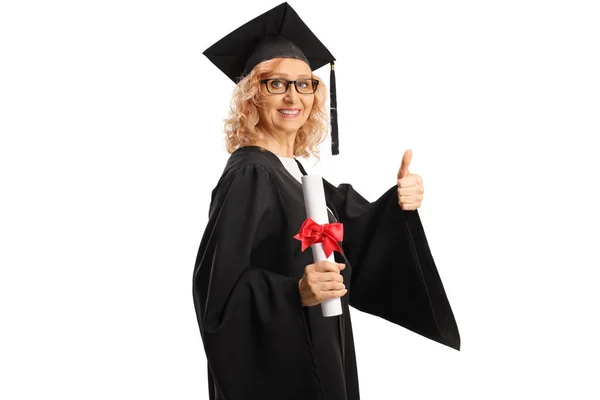 卒業生のガウンに身を包んだ熟女が卒業証書を持ち 親指を白い背景に隔離 — ストック写真