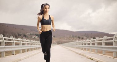 Genç bir kadın köprüde koşuyor.