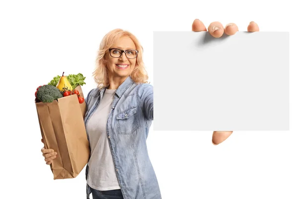 袋の笑顔と白い背景に隔離された空白のカードを示す食料品の袋を持つ熟女 — ストック写真