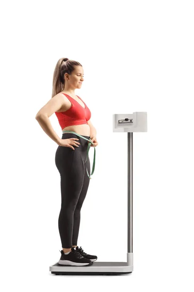 スポーツウェアを着た若い女性が体重計の上に立ち 白い背景に隔離された腰を測定する — ストック写真