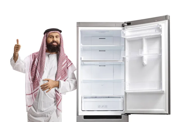 stock image Sudi arab man leaning on an empty  open fridge and showing thumbs up isolated on white background