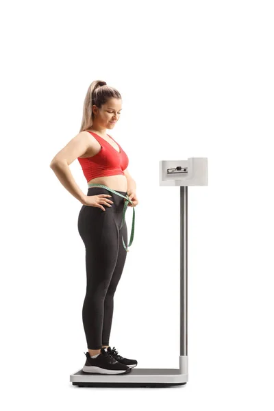 スポーツウェアを着た若い女性が体重計に立って 白い背景に隔離された腰を測定します — ストック写真