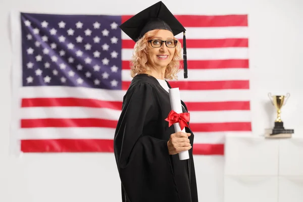 アメリカ国旗の前で修士号を取得した黒の卒業生のガウンを着た女性 — ストック写真