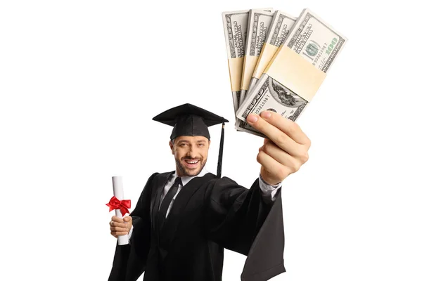 卒業のガウンを着て卒業証書を保持し 白い背景に隔離されたお金の山を示す男性学生 — ストック写真
