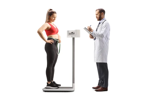 白地に隔離されたスポーツウェアで若い女性の医師の重量をチェック — ストック写真