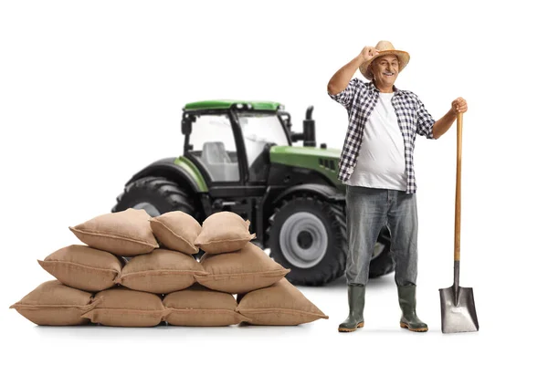 白の背景に隔離された帽子でシャベルと緑のトラクター挨拶を持つ成熟した農家 — ストック写真