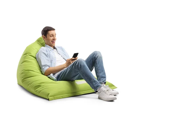 Ung Man Sitter Bönpåse Skrattar Och Tittar Smartphone Isolerad Vit — Stockfoto