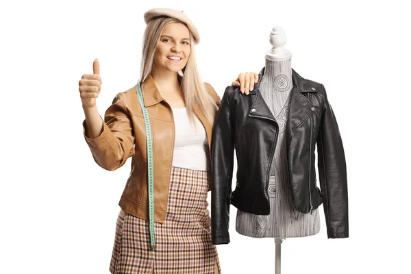 若い女性のファッションデザイナーは 革のジャケットとジェスチャー親指を持つマネキン人形にもたれて白の背景に隔離された — ストック写真