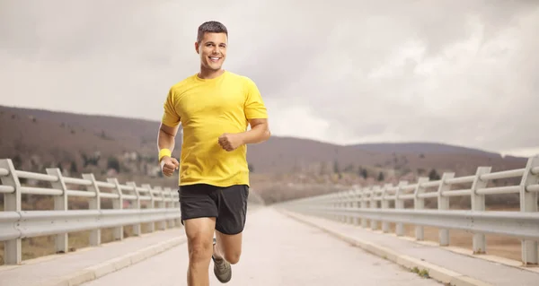 Spor Kıyafetli Genç Adam Köprüde Koşuyor Gülümsüyor — Stok fotoğraf