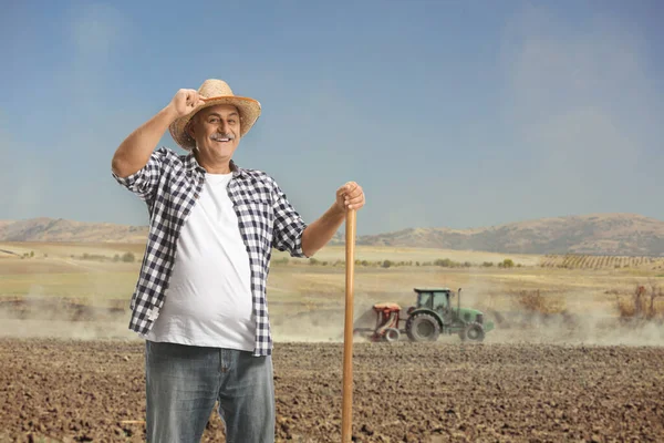 一个快乐的成熟农民的画像 他拿着铲子站在尘土飞扬的田里 拖着拖拉机 — 图库照片