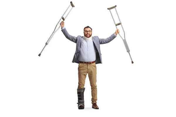 幸せな男とともに子宮頸部襟と整形外科ブーツ持ち上げる松葉杖隔離された上の白い背景 — ストック写真