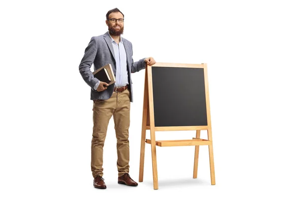 一个留着胡子的男教师站在一块黑板旁边 手里拿着用白色背景隔开的书 他的全长画像 — 图库照片