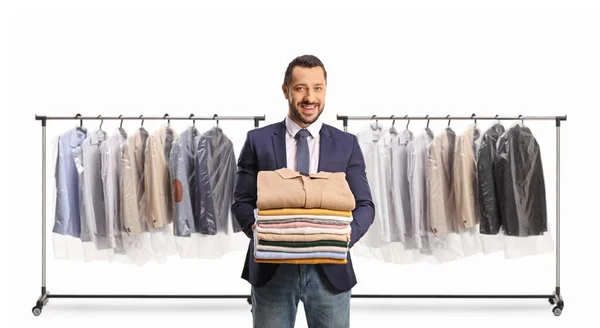 白い背景に隔離された衣類棚の前に折り畳まれた服の山を保持ドライクリーナーで男性の顧客 — ストック写真