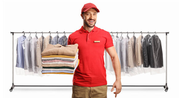 Male worker holding a pile of folded clothes in front of clothing racks at dry cleaners isolated on a white backgroun