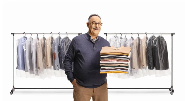 Fröhlicher Älterer Mann Mit Einem Stapel Zusammengefalteter Kleidung Vor Regalen — Stockfoto