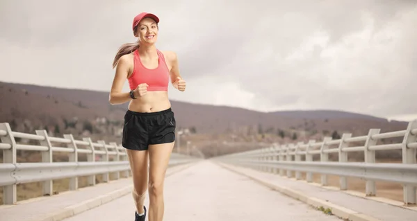 年轻的微笑女子穿着运动服在桥上慢跑 — 图库照片