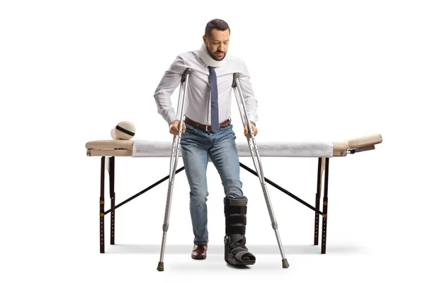 Portret Mężczyzny Ortopedycznym Bucie Spacerującego Kulami Przed Łóżkiem Terapeutycznym Odizolowanego — Zdjęcie stockowe