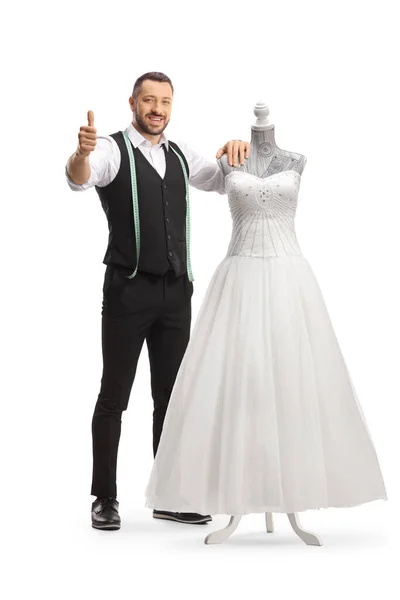 裁缝站在穿着洋娃娃模特礼服的婚纱旁边 给被白色背景隔开的大拇指做手势 — 图库照片