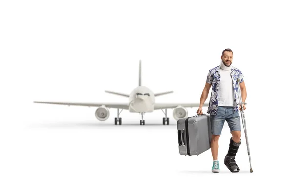 白い背景に隔離された飛行機の前でスーツケースを保持整形外科のブーツと子宮頸部の襟を持つ乗客 — ストック写真