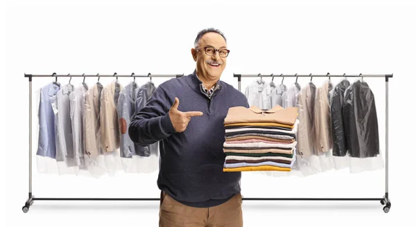 Cheerful Mature Man Holding Pile Folded Clothes Pointing Front Racks — Stock Photo, Image